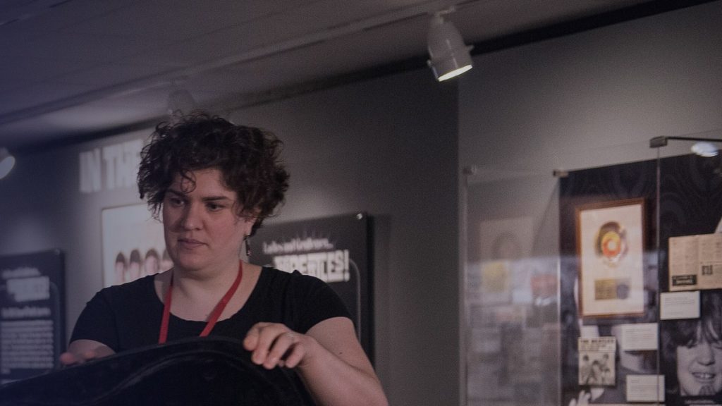 A woman with a staff lanyard prepares an exhibit in a museum gallery