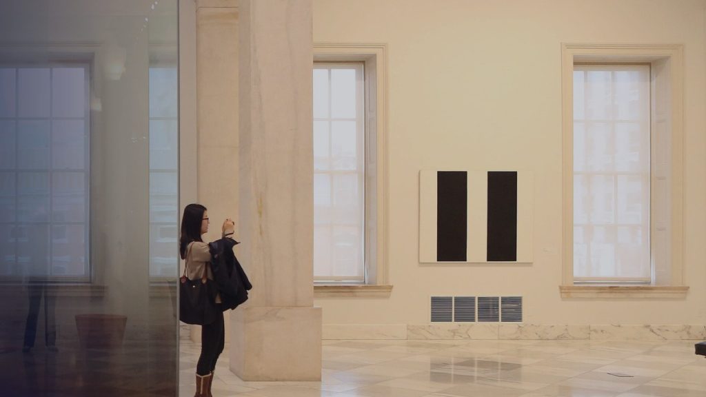A visitor photographs a painting in a bright museum hall