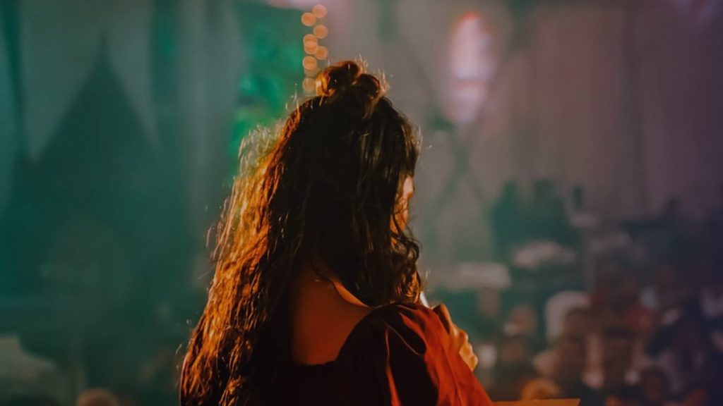 A performer seen from behind, facing an audience under stage lights